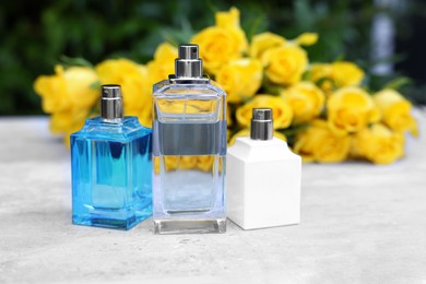 Photo of Perfumes and beautiful bouquet of yellow roses on light table outdoors, selective focus