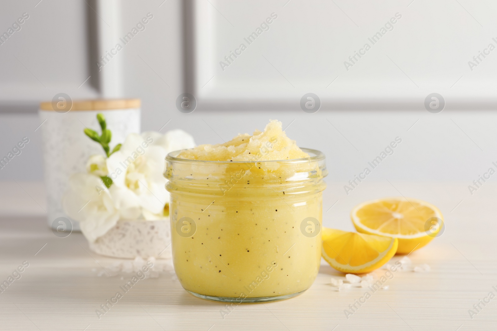 Photo of Body scrub in glass jar, freesia flowers and lemon on wooden table