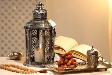 Photo of Arabic lantern, Quran, misbaha and dates on white table