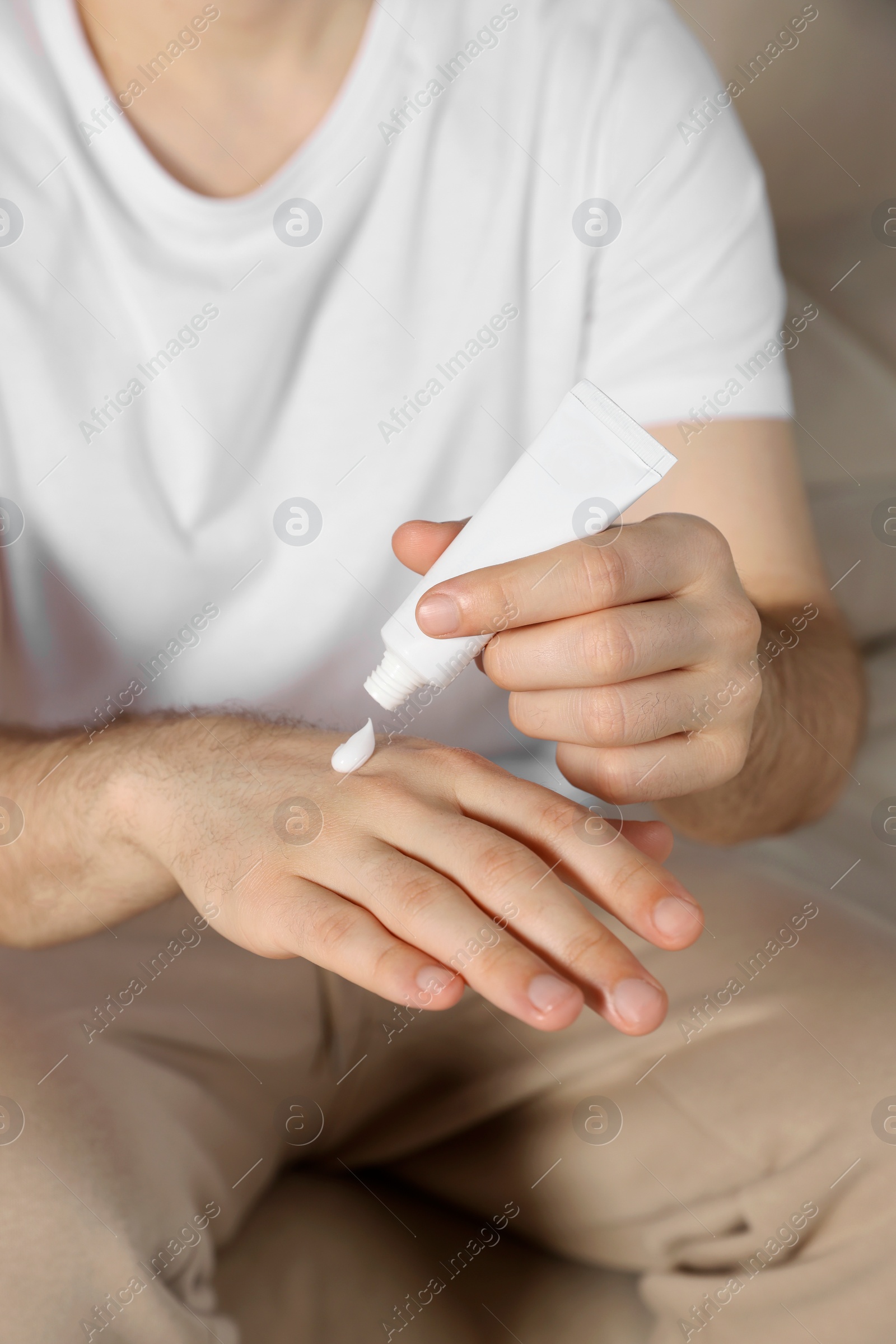 Photo of Man applying cream onto hand at home, closeup