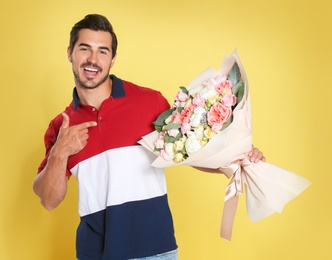 Young handsome man with beautiful flower bouquet on yellow background