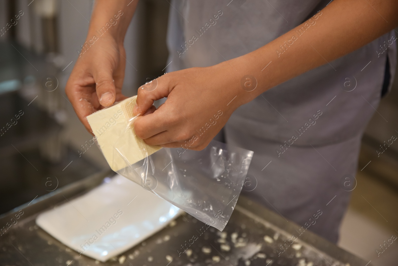 Photo of Worker packaging feta cheese at modern factory, closeup