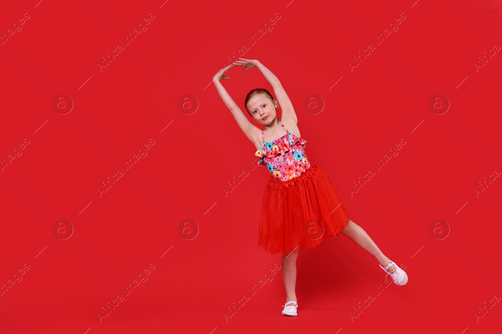 Photo of Cute little girl dancing on red background, space for text