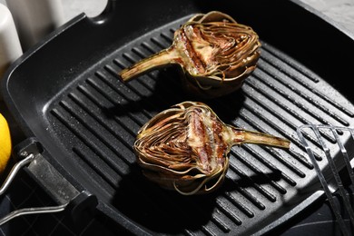 Photo of Tasty grilled artichokes in pan on table, closeup