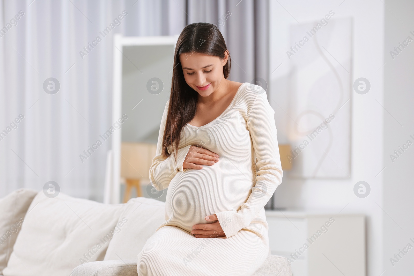 Photo of Beautiful pregnant woman sitting on sofa at home