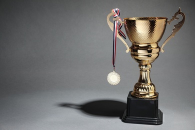 Photo of Golden trophy cup and medal on grey background. Space for text