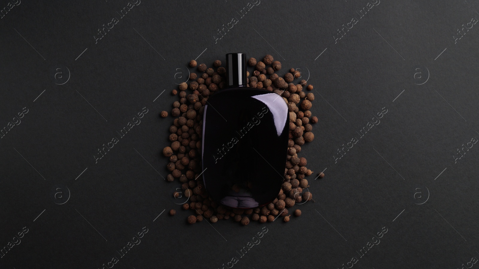 Photo of Bottle of perfume surrounded by allspice on dark background, top view