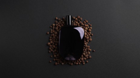 Photo of Bottle of perfume surrounded by allspice on dark background, top view