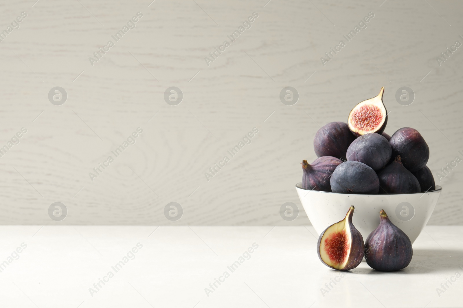 Photo of Whole and cut tasty fresh figs on white table. Space for text