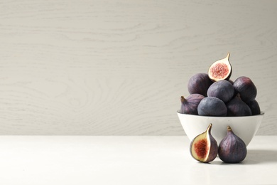 Whole and cut tasty fresh figs on white table. Space for text