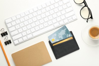 Photo of Leather card holder with credit cards, glasses, keyboard, coffee and stationery on white table, flat lay