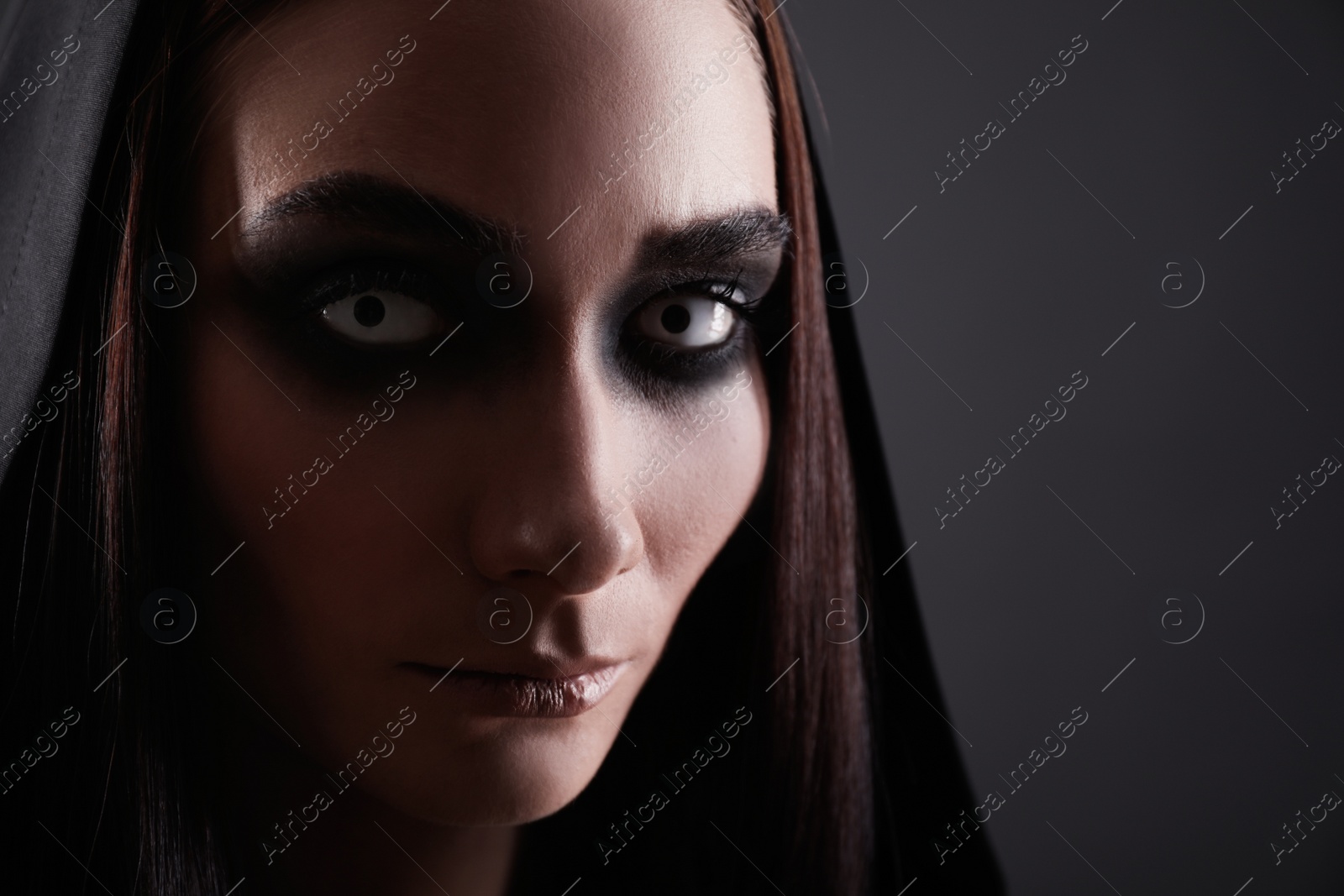 Photo of Mysterious witch with spooky eyes on black background, closeup