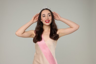 Photo of Beautiful young woman with tiara and ribbon in dress on grey background. Beauty contest