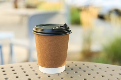 Photo of Paper cup with hot coffee on table outdoors, closeup. Takeaway drink