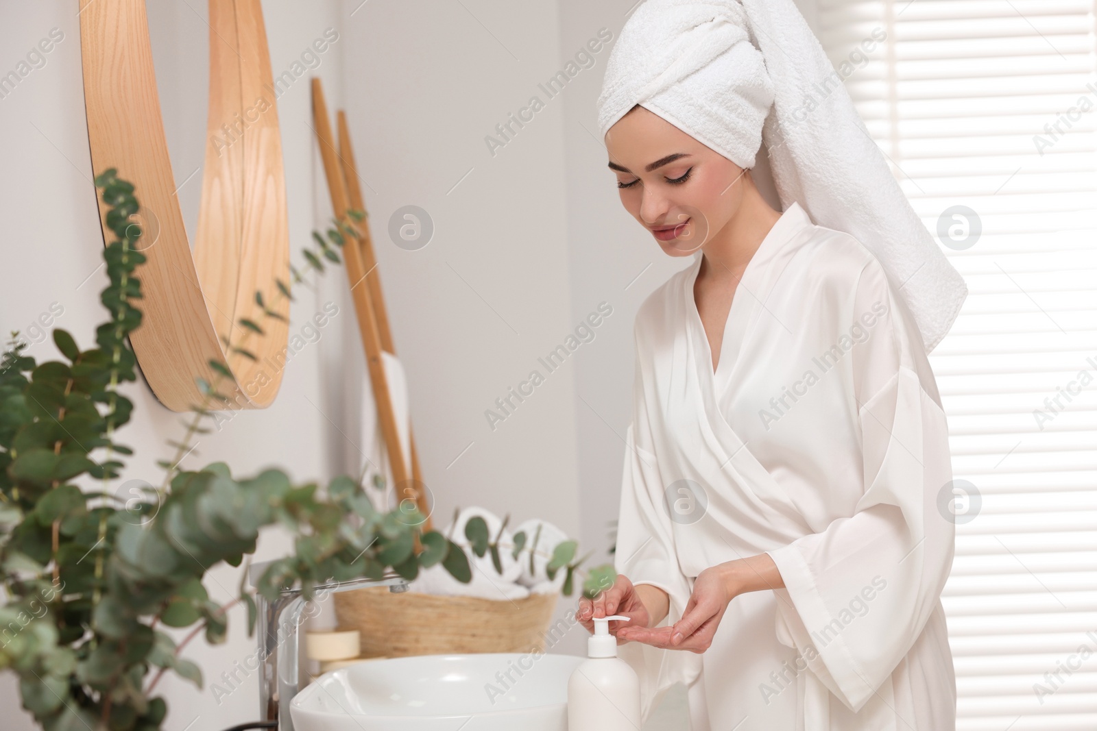 Photo of Beautiful young woman using body cream in bathroom, space for text