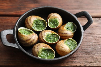 Delicious cooked snails in baking dish on wooden table, closeup