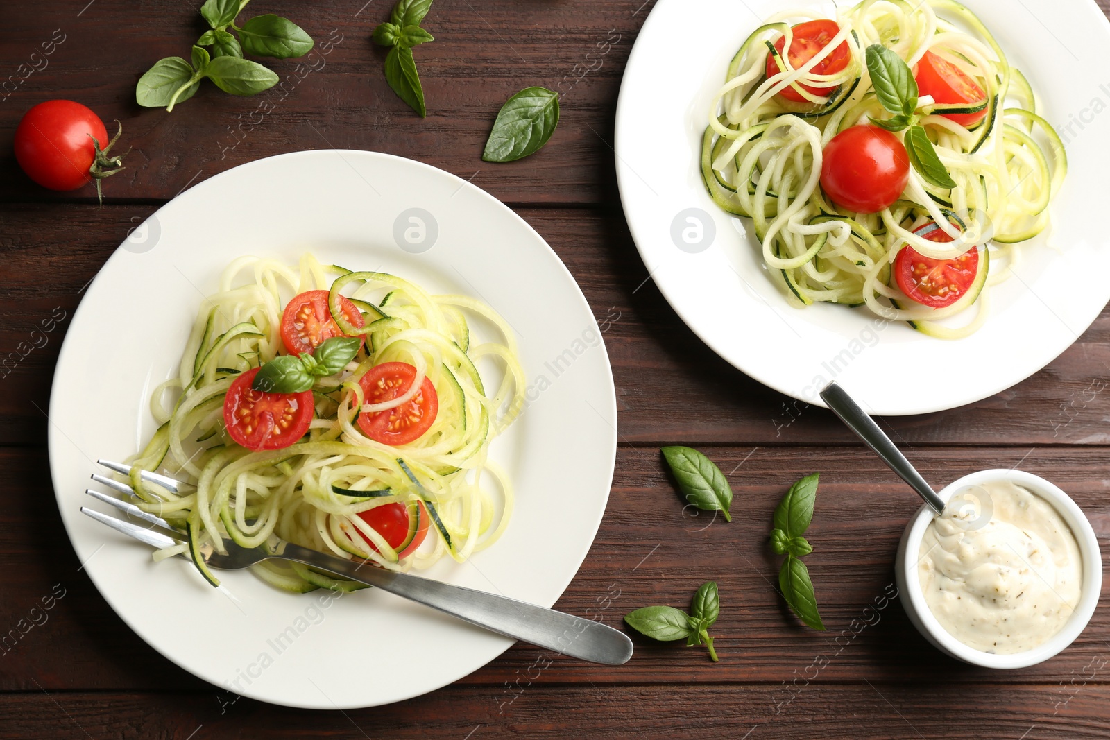 Photo of Tasty zucchini pasta with tomatoes and basil served on wooden table, flat lay