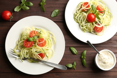 Photo of Tasty zucchini pasta with tomatoes and basil served on wooden table, flat lay