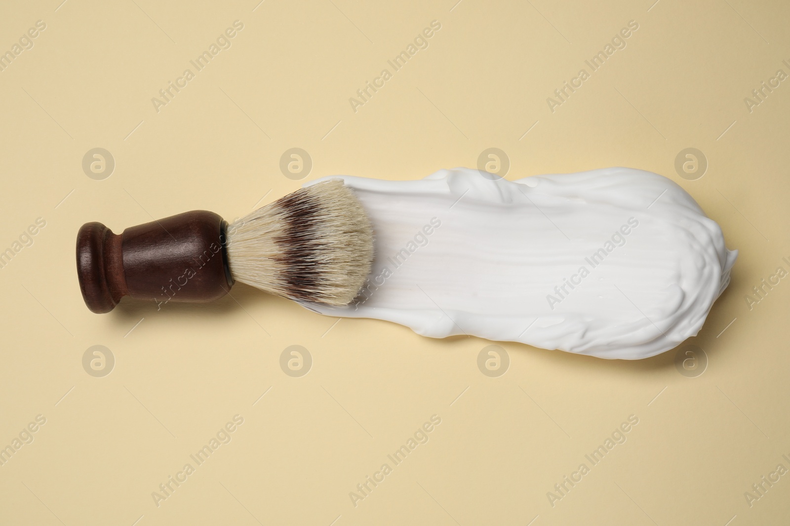 Photo of Brush with shaving foam on beige background, top view