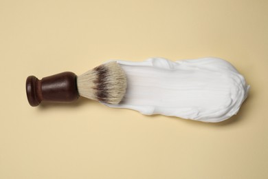 Brush with shaving foam on beige background, top view