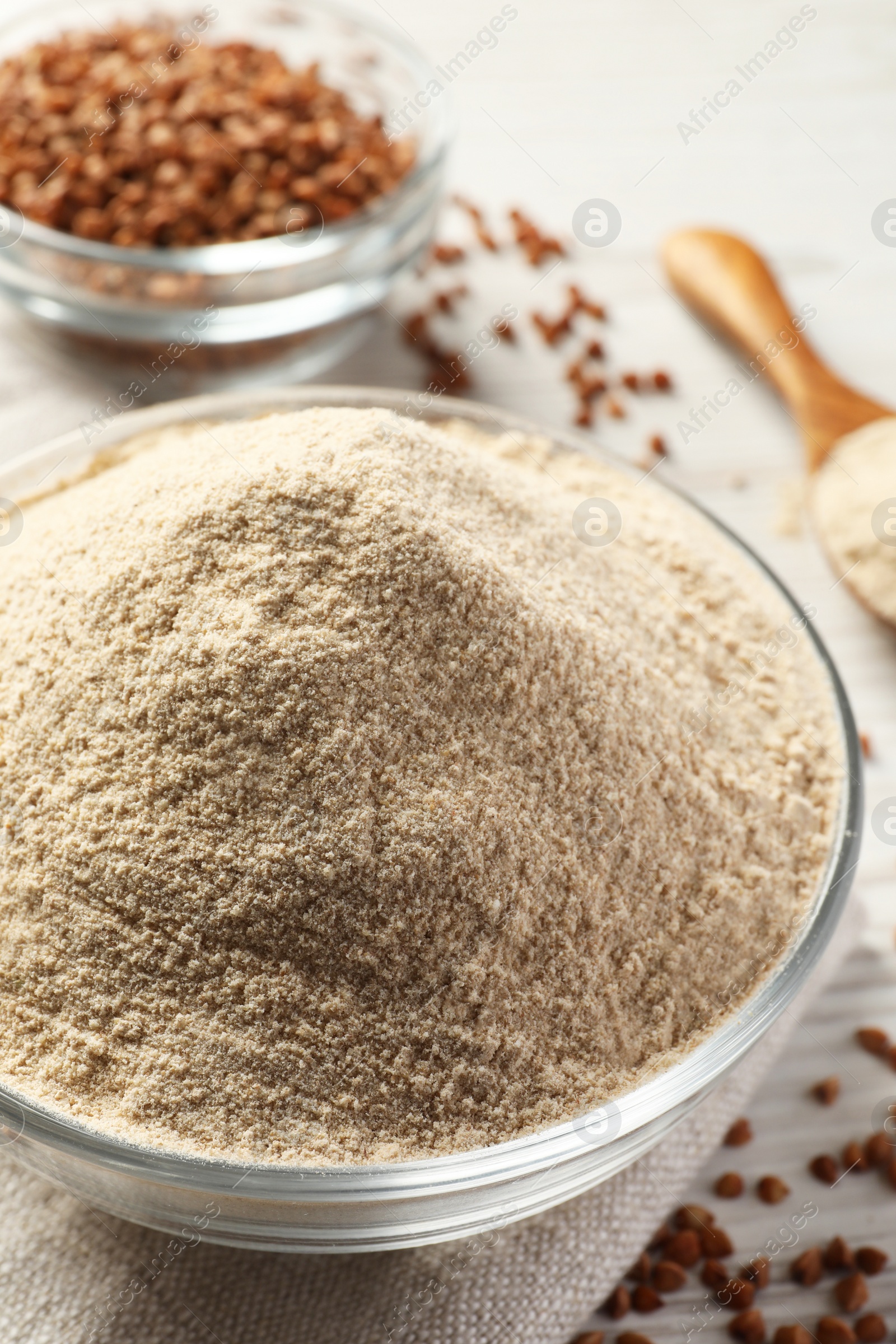 Photo of Glass bowl of buckwheat flour and cloth on white table, closeup