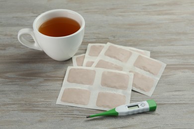 Photo of Mustard plasters, cup of tea and thermometer on wooden table