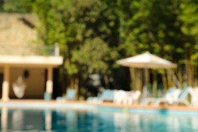 Photo of Blurred view of clear pool, sunbeds and umbrella outdoors