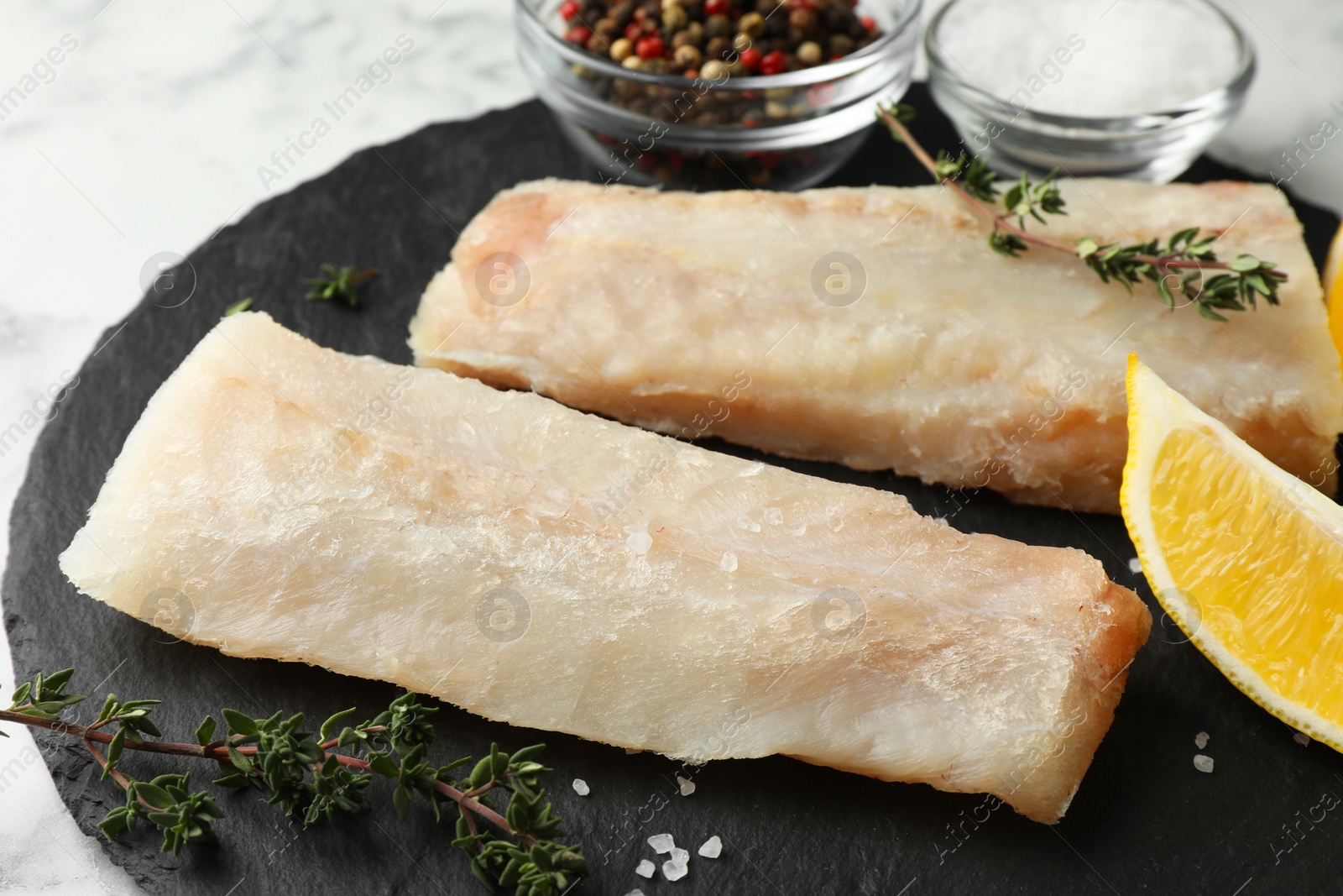 Photo of Fresh raw cod fillets, spices and lemon on white table, closeup