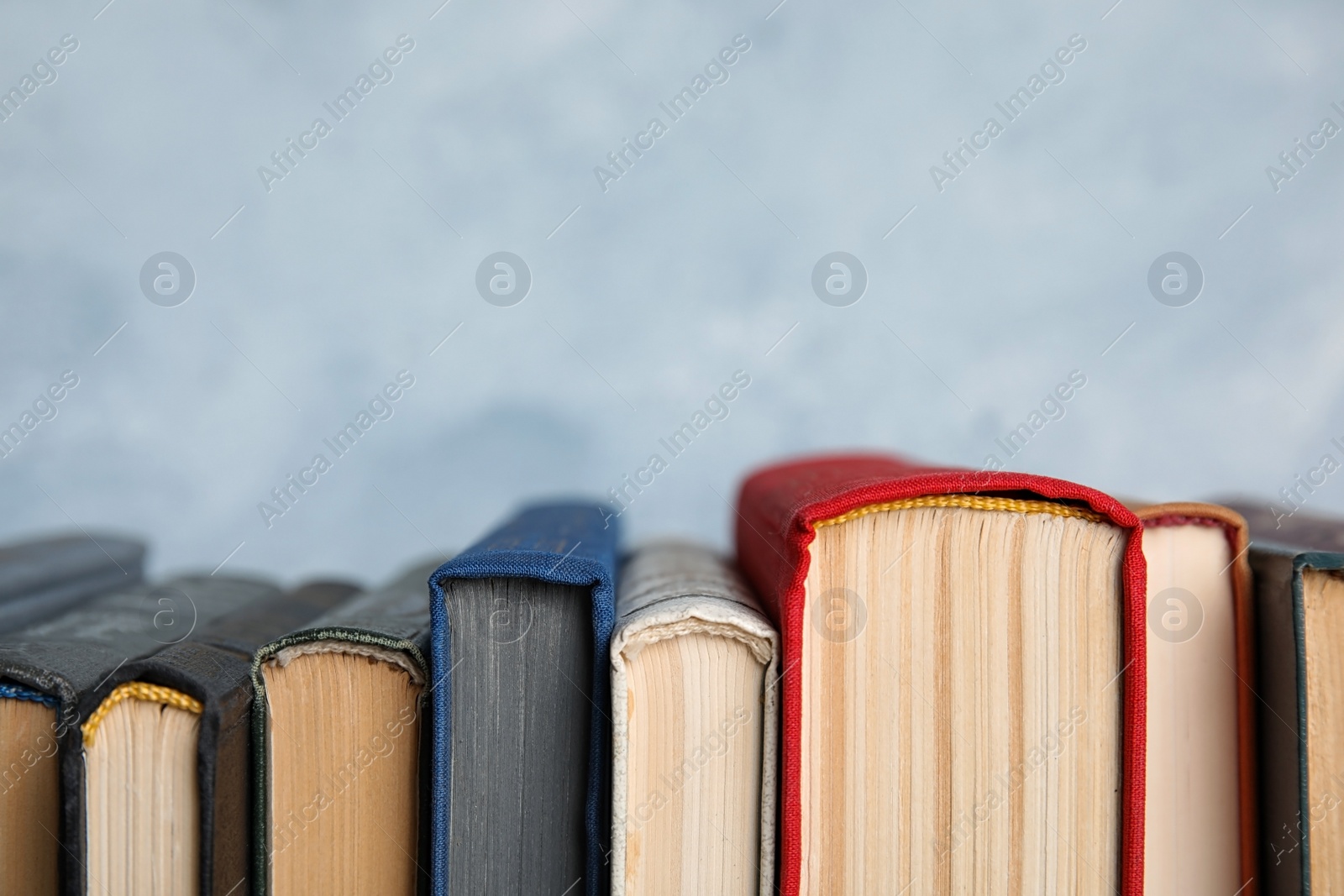 Photo of Stack of hardcover books on light blue background, closeup. Space for text