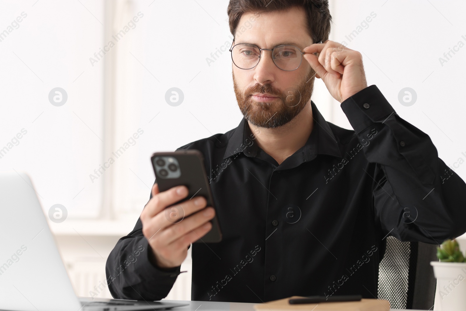 Photo of Handsome man using smartphone at table in office