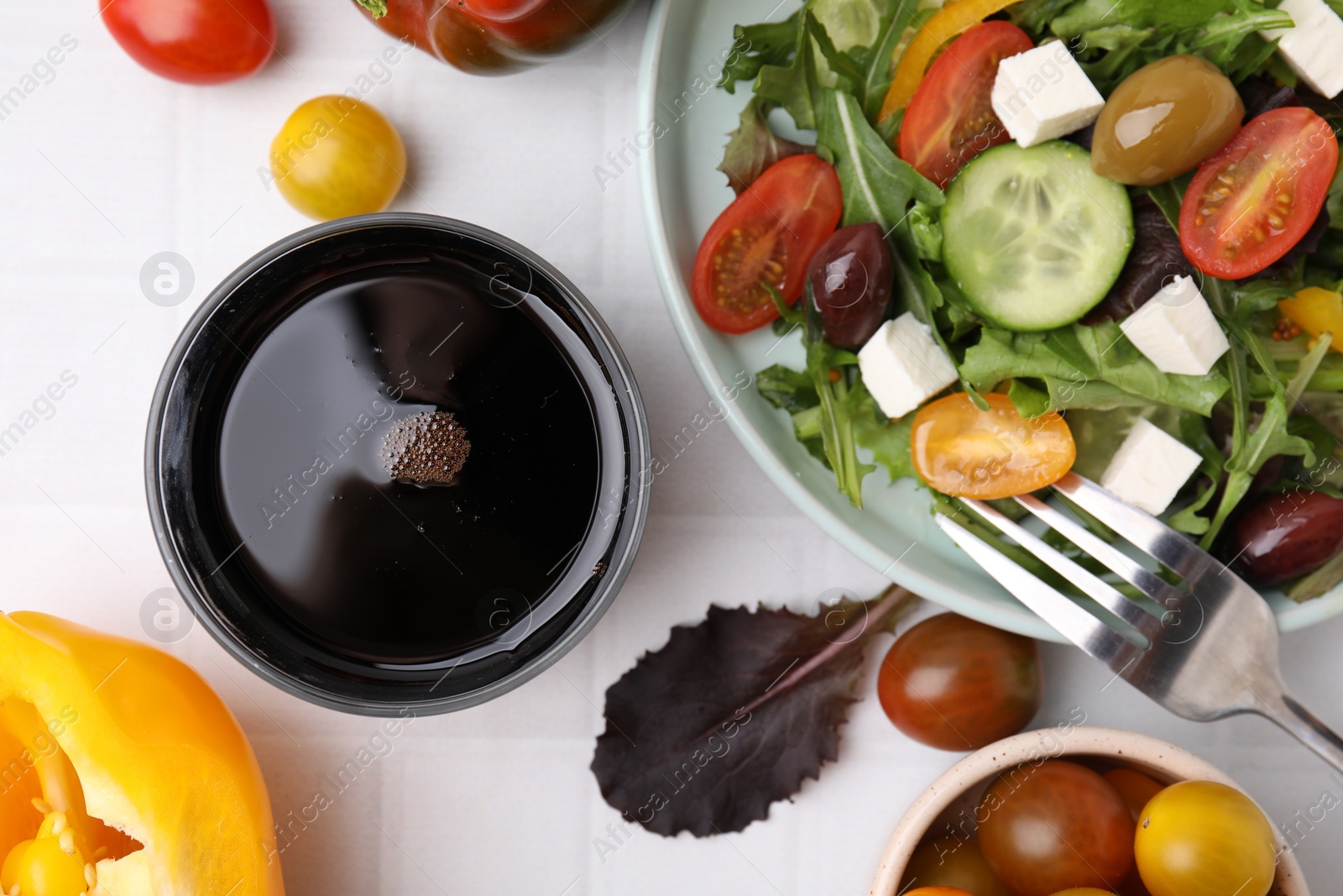 Photo of Vinegar in glass, salad and products on white tiled table, flat lay