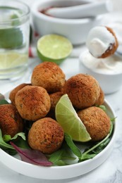 Photo of Delicious falafel balls with herbs and lime on white table, closeup