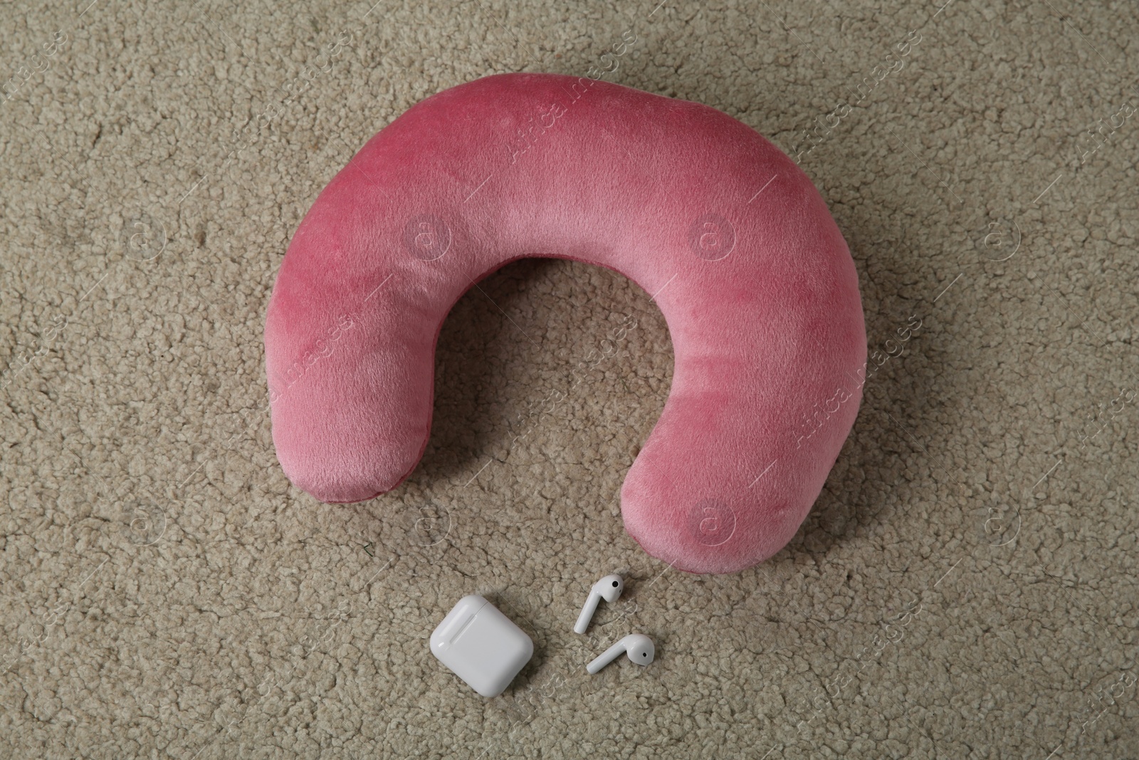 Photo of Pink travel pillow and earphones on beige rug, flat lay