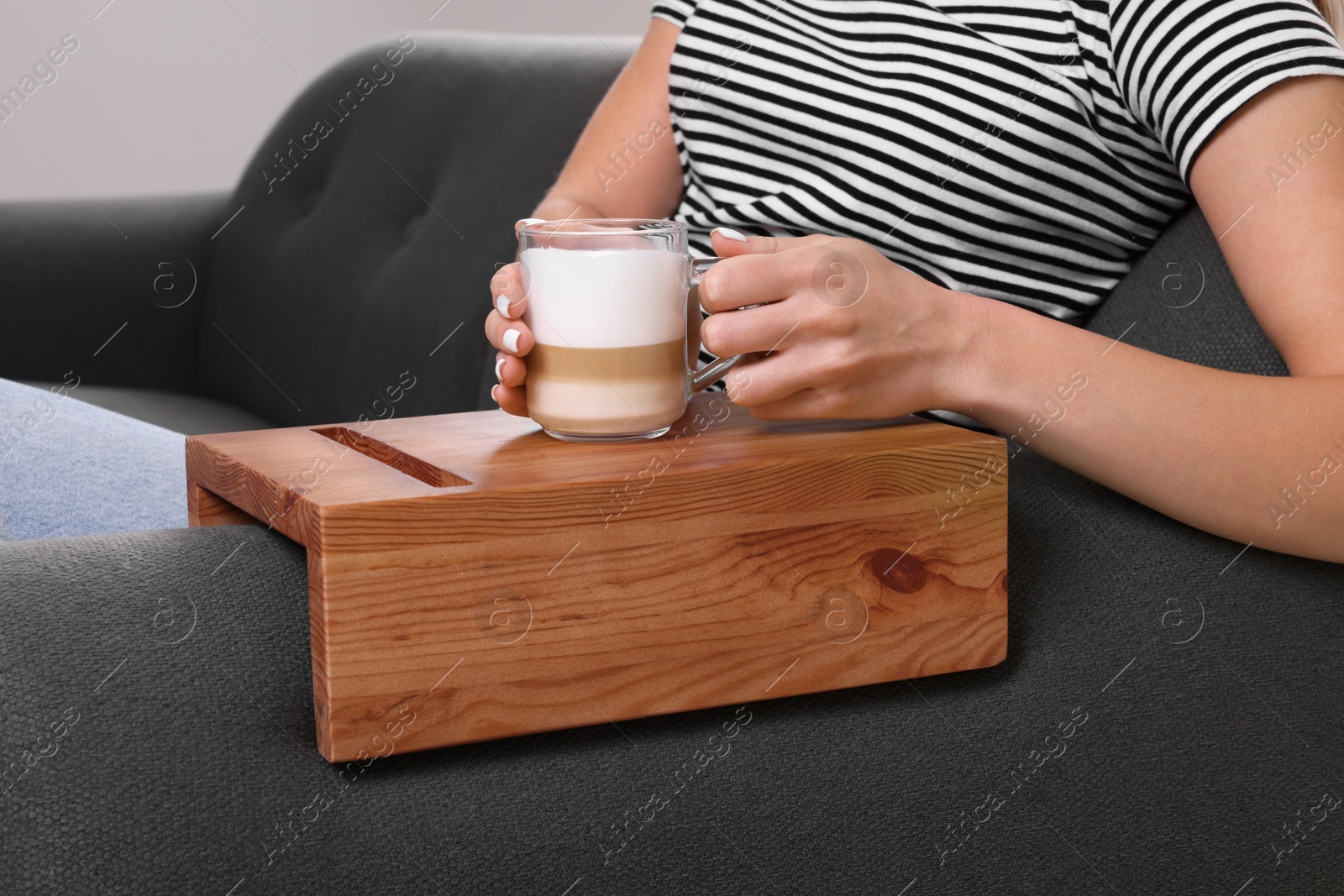 Photo of Woman holding cup of coffee on sofa armrest wooden table at home, closeup