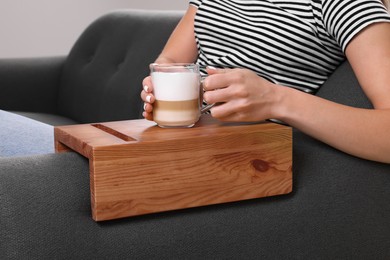 Woman holding cup of coffee on sofa armrest wooden table at home, closeup