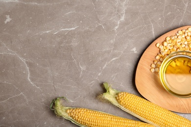 Photo of Flat lay composition with bowl of corn oil, cobs and kernels on gray background