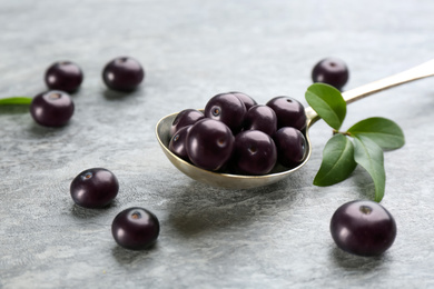 Photo of Fresh acai berries and spoon on light grey table, closeup