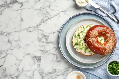 Delicious bagel with cream cheese and green onion on white marble table, flat lay. Space for text