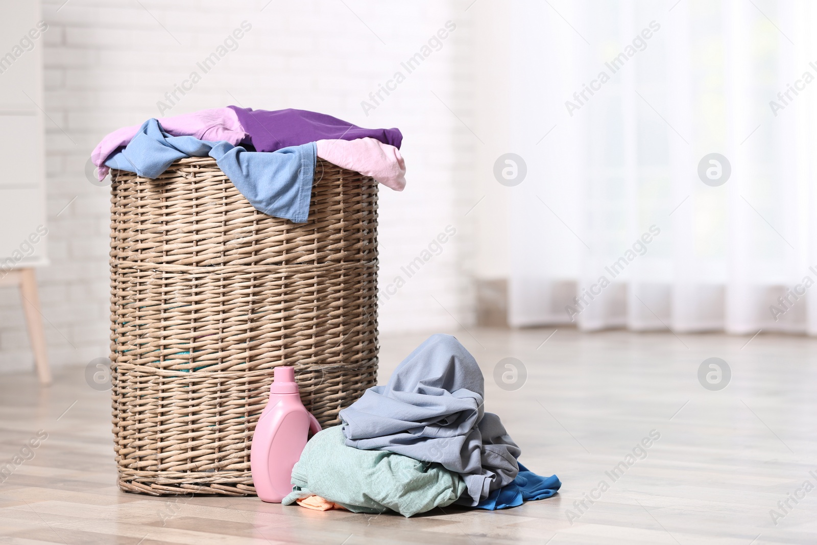 Photo of Wicker laundry basket with dirty clothes and detergent on floor indoors. Space for text
