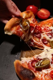 Woman taking piece of delicious pizza Diablo on black background, closeup