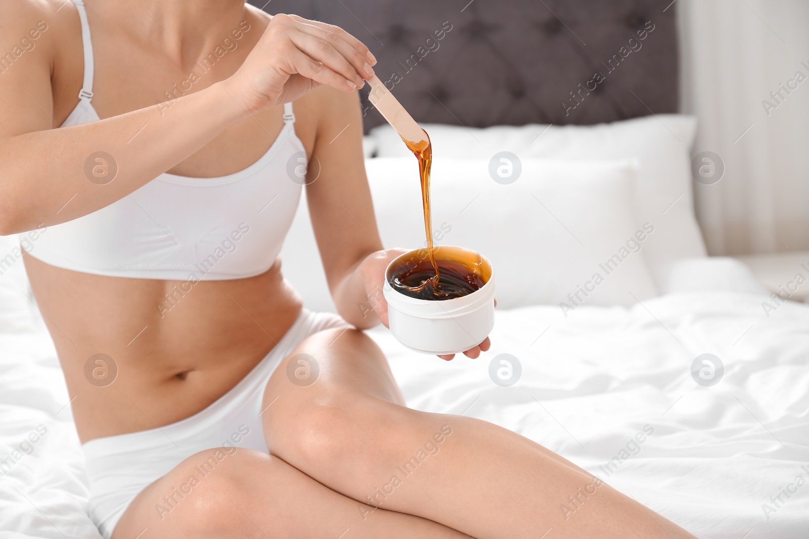 Photo of Woman holding hot wax on bed at home, closeup. Epilation procedure