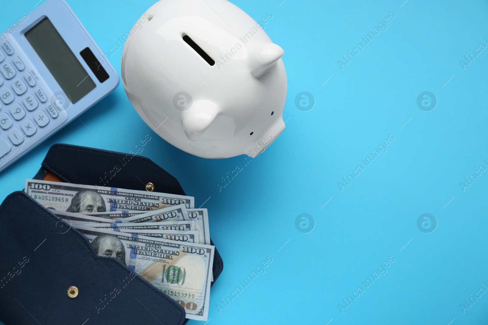 Photo of Piggy bank, calculator and wallet with banknotes on light blue background, flat lay. Space for text