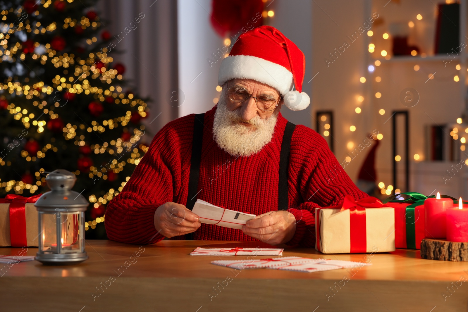 Photo of Santa Claus reading letter at his workplace in room decorated for Christmas