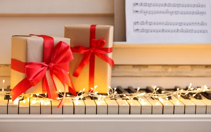 Photo of Gift boxes and fairy lights on piano keys, closeup. Christmas music