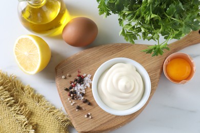 Tasty mayonnaise sauce in bowl, ingredients and spices on white table, flat lay