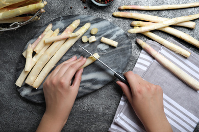 Photo of Woman cutting fresh white asparagus at grey table, top view