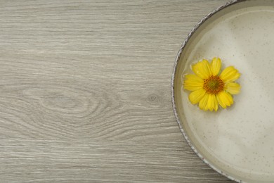 Photo of Beige bowl with water and yellow flower on wooden table, top view. Space for text