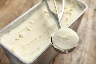 Container and scoop with delicious vanilla ice cream on wooden table, closeup