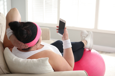 Lazy overweight woman using smartphone instead of morning training