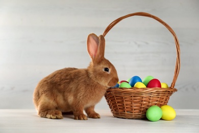 Photo of Cute bunny and basket with Easter eggs on white table